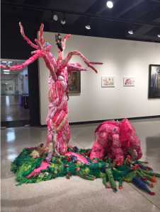 A large scale mixed media sculpture by Kelly Boehmer of an elephant-like creature standing under a tree.