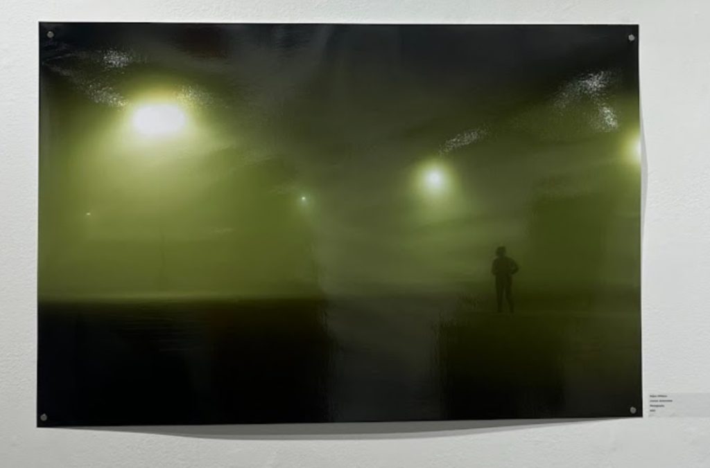 Large poster print of a green smoke-y empty parking lot where Williams stands alone in the late hours of the night