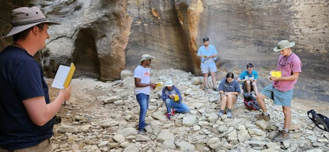 A student delivers a presentation to other students within a slot canyon at Zion National Park